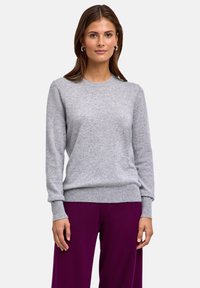 Hellgrauer Strickpullover mit langen Ärmeln, rundem Ausschnitt und gerippten Bündchen sowie Saum, kombiniert mit lila weiten Hosen.