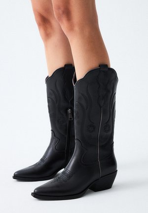 Botas de vaquero negras de cuero, con patrones florales en relieve, punteras apuntadas y un tacón bajo apilado, con cierre de cremallera en el lateral.