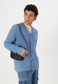 Μπλε, φουντωτός καρφίτσας με V-ντεκολτέ, πέντε κουμπιά και μακριά μανίκια. Συνδυάζεται με μια μικρή μαύρη τσάντα ώμου και τζιν παντελόνι.