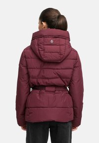 Bordo armēta jaka ar pieguļošu vidukli, lielu kapuci un logo detaļu aizmugurē. Iezīmēts ar quilted tekstūru un izturīgu audumu.