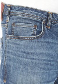 Jeans in denim blu chiaro con una sottile trama, caratterizzati da un classico design a cinque tasche e una toppa in pelle marrone nella vita.