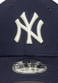 Gorra de béisbol azul marino de tela, con un logotipo bordado en color crema "NY" en el frente y una correa ajustable en la parte posterior.
