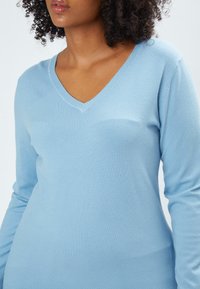 Pullover lungo azzurro chiaro a maniche lunghe con scollatura a V e texture morbida, che offre una silhouette aderente e un design minimalista.