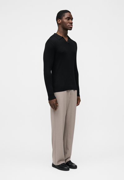 Polo à manches longues côtelé noir avec col en V, associé à un pantalon large beige clair et des chaussures noires. Texture du tissu lisse.