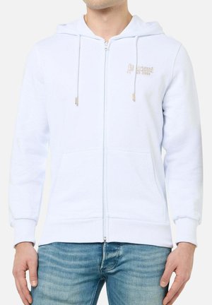 Mann trägt weißen Kapuzenpullover mit Reißverschluss vorne und Taschen sowie hellblaue Jeans, steht mit entspannt an den Seiten hängenden Händen.