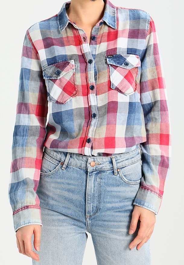 Personne portant une chemise à carreaux rouge, bleue et blanche à manches longues, rentrée dans un jean taille haute bleu clair.