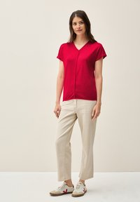 Top corto rojo de manga corta con escote en V, combinado con pantalones beige claros y zapatillas blancas con detalles rojos. Diseño simple y casual.