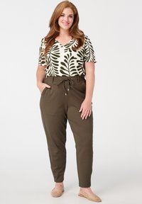 Haut crème à manches courtes avec un motif floral et des feuilles vertes. Pantalons olive avec cordon de serrage. Chaussures à enfiler tressées couleur sable.