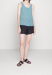 Top senza maniche turchese con un motivo a pois, abbinato a pantaloni corti scuri e sandali neri. Design semplice, tessuto casual e colori pieni.