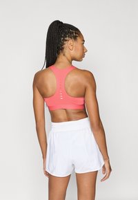 Κοραλί αθλητικό σουτιέν με σχέδιο racerback, που διαθέτει οριζόντια κοψίματα, σε συνδυασμό με λευκό σορτς με ελαστική μέση.