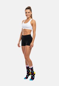 Sorte træningsshorts og en hvid crop top, parret med sorte sokker med farverige prikker og klare blå og gule accenter.