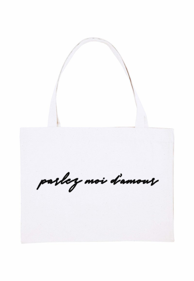 Borsa tote bianca in tela con due manici robusti e testo in corsivo nero "parlez moi d'amour" sul davanti.