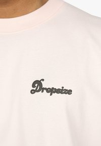 Lyserød bomulds t-shirt med et sort, stiliseret "Dropsize" logo. Rundhalsen har en kontrasterende ribkant.