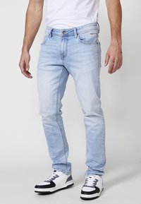 Jeans de denim azul claro con corte ajustado, que cuentan con cinco bolsillos, cremallera en la bragueta y costuras en contraste. Combinados con zapatillas blancas y negras.