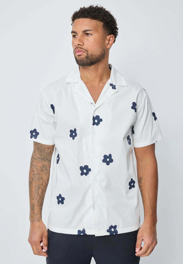 Chemise à manches courtes en coton blanc avec des motifs de fleurs bleu foncé, dotée d'un col et de boutons à l'avant. Tissu texturé avec une coupe décontractée.