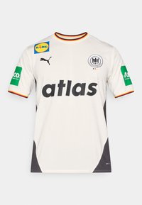 Balta sporta krekls ar melniem akcentiem, uz kura ir uzraksts "atlas" biezos burtiem, Puma logo un dažādi krāsaini sponsoru plāksteri uz piedurknēm un krūtīm.