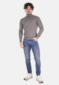 Maglione a collo alto grigio, vestibilità slim, abbinato a jeans in denim blu. Sneakers bianche con dettagli grigi. Design semplice e moderno, texture liscia.