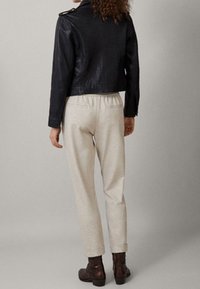 Schwarze Lederjacke im Cropped-Stil mit Schulterepauletten, kombiniert mit beigen Sweatpants und braunen Knöchelstiefeln, von hinten betrachtet.