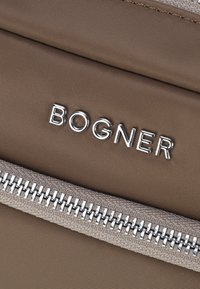 Bolsa de tela marrón con un logo plateado "BOGNER", textura suave y una cremallera beige con detalles de dientes metálicos.