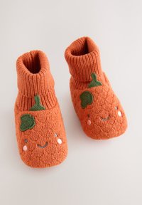 Chaussons tricotés orange avec un bord côtelé, ornés de motifs de feuilles vertes et de détails faciaux brodés en rose et bleu. Texture douce.