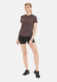 Bruine sportieve t-shirt met korte mouwen, gladde textuur, gecombineerd met zwarte aansluitende shorts en zwarte sport schoenen. Eenvoudig ontwerp, minimale branding.