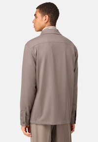 Brun, lätt jacka med klassisk krage, långa ärmar och knappade muddar. Slät textur, enkel design med en avslappnad passform.