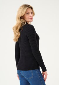 Black, ribbed long-sleeve sweater with a fitted design and round neckline, paired with blue jeans. Smooth texture, no visible patterns or accents.
