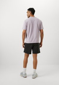 Lilac cotton t-shirt with short sleeves and a back seam, paired with dark grey shorts. Model also wears white socks and light grey sneakers.