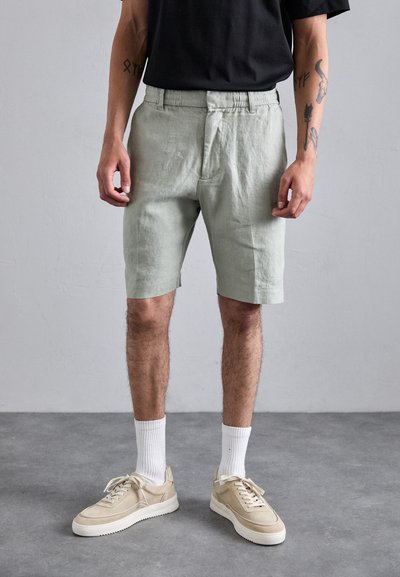 Shorts en lin vert clair à coupe décontractée avec une taille élastique, associés à des baskets beiges et des chaussettes blanches mi-mollet.