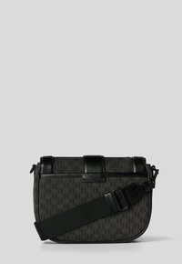 Svart och grå crossbody-väska med en texturerad yta, som har en elegant design, justerbar rem, två övre lås och en logodetalj.