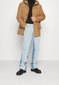 Brauner Wollmischung-Dufflecoat mit Toggle-Verschlüssen, schwarzem Rollkragenpullover, hellblauen Jeans mit dunkleren Seitenelementen und schwarzen Stiefeletten.