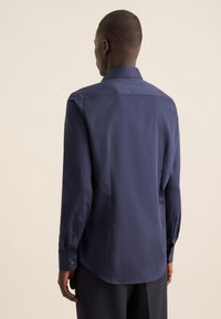 Marineblauwe blouse met lange mouwen, met een knoopsluiting kraag, gladde stof, achterste yoke-detail en een afgeronde zoom. Knoopaccenten bij de manchetten.