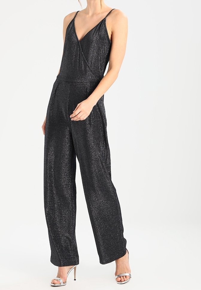 Svart, glittrande jumpsuit med V-hals, tunna axelremmar och vida ben; har en omlottskärning i bodice och en slät yta. Matchas med silverfärgade klackar.
