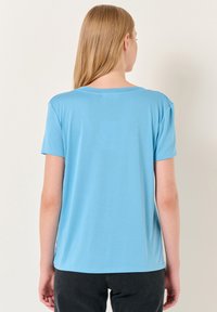 Jasnoniebieska koszulka z krótkim rękawem i okrągłym dekoltem. Gładki, miękki materiał, prosty krój oraz minimalistyczny design bez wzorów czy akcentów.