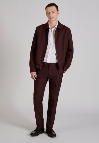 Chaqueta burdeos a medida con botones sobre una camisa blanca, combinada con pantalones a juego y zapatos de cuero negros. Tejido liso, corte estructurado.