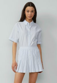 Lichtblauwe jurk met kraag, korte mouwen, geplooide rok en elastische tailleband. Bevat knoopdetails aan de voorkant.