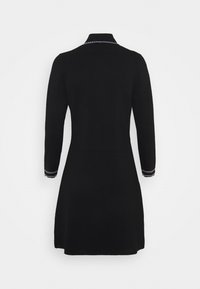 Robe noire à manches longues, col structuré et surpiqûres blanches contrastantes aux poignets. Silhouette ajustée se rétrécissant à la taille.