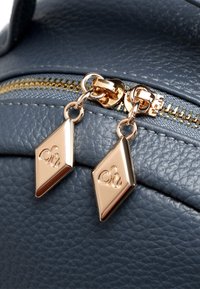 Grijze leren tas met textuur en een gouden rits. Twee ritskruidjes in de vorm van een diamant hebben gegraveerde accenten die het ontwerpdetail verbeteren.