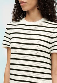 Pull court à manches courtes en maille avec un motif rayé crème et vert foncé. Il présente un point texturé et un col rond.