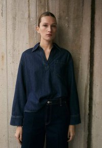 Chemise en denim bleu foncé avec un col, des manches longues et une poche poitrine, assortie à un pantalon en denim foncé.