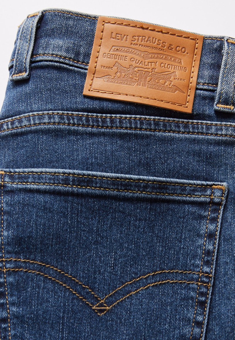 Jean en denim bleu foncé avec des coutures orange, présentant une patch en cuir portant l'inscription "Levi Strauss & Co." au dos de la taille.