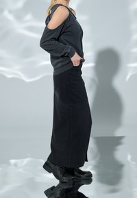 Sweat-shirt noir surdimensionné avec épaules découpées, associé à une jupe en denim noire. Des bottes noires épaisses complètent le look, mettant en valeur un style décontracté.