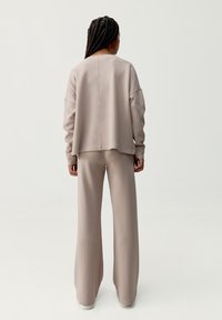 Felpa oversize beige e pantaloni a gamba larga abbinati, realizzati in tessuto morbido. Presenta spalle scese e una vestibilità rilassata.