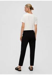Witte T-shirt met korte mouwen gecombineerd met zwarte elastische broek met een taps toelopend ontwerp, gedragen met zwarte sandalen.