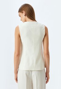Witte mouwloze top met een hoge halslijn, gestructureerd ontwerp en een gladde textuur, met een centrale naad aan de achterkant en zonder zichtbare versieringen.
