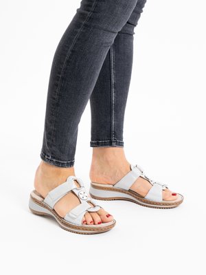 Voeten met witte verstelbare sandalen en rode teennagellak, gecombineerd met donkere skinny jeans tegen een witte achtergrond.