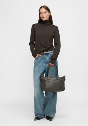 Brązowy golf, jasnoniebieskie szerokie dżinsy, trzymająca ciemnozieloną skórzaną torebkę z srebrnymi elementami i teksturowanym wzorem.