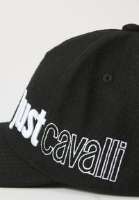 Gorra negra hecha de material de fieltro con texto blanco bordado "Just Cavalli" en la parte frontal. Visera curvada con una superficie texturizada.