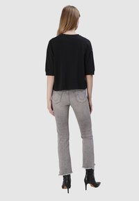 T-shirt noir court à manches courtes, assorti à un jean gris clair délavé avec des ourlets effilochés et des bottines à talons hauts noires.