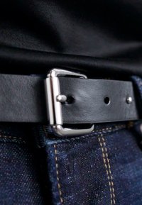 Ceinture en cuir noir avec une boucle en métal argenté, présentant une texture lisse et des trous pour l'ajustement, portée sur un tissu en denim foncé.